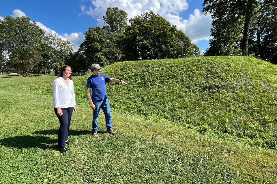 A woman and a man stand next to a swell of earth on a sunny day.