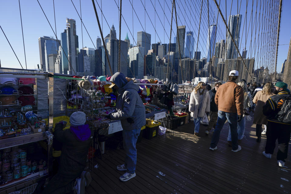 Pedestrians pass by vendors on the Brooklyn Bridge in New York, Tuesday, Jan. 2, 2024. New York City will ban vendors from the Brooklyn Bridge starting Wednesday, Jan. 3, 2024. The move is intended to ease overcrowding on the famed East River crossing, where dozens of souvenir sellers currently compete for space with tourists and city commuters. (AP Photo/Seth Wenig)