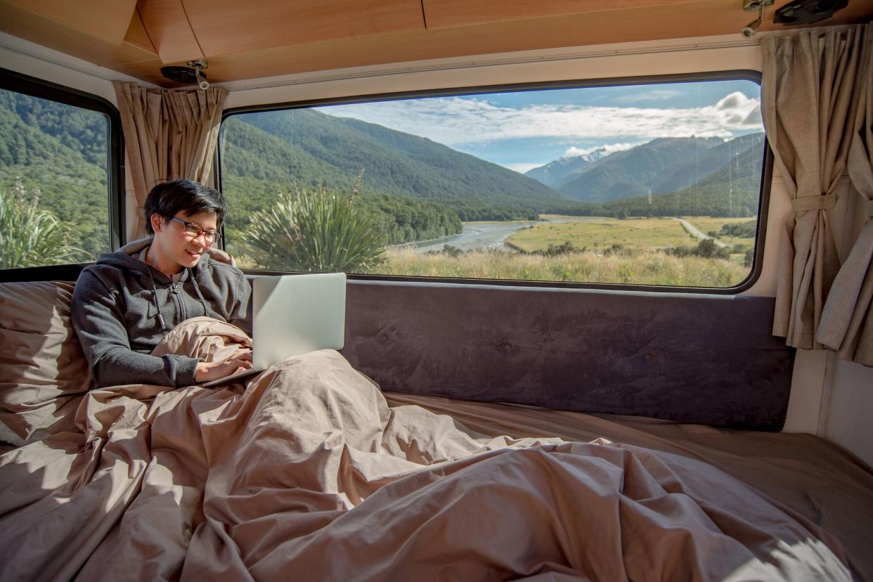 young Asian man working with laptop computer on the bed in camper van