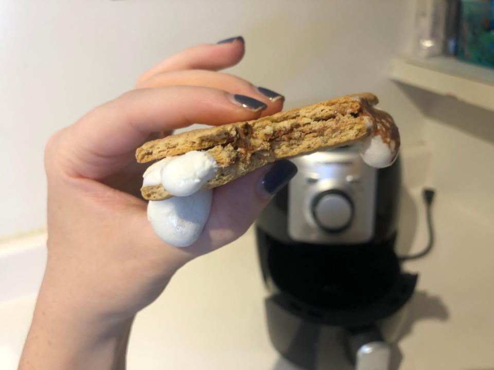 hand holding air-fried smore with marshmallow dripping out in front of an air fryer