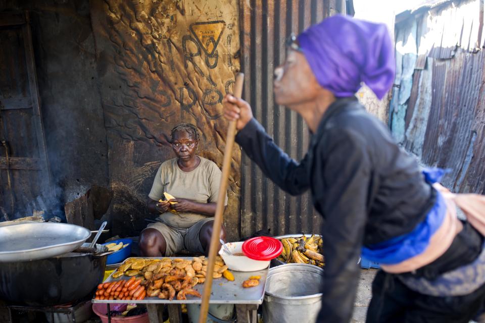 In this Oct. 27, 2018 photo, Atesi Auguste, a voodoo priestess, sits as she sells fried meat and bananas and she watches Mimose Bernard who issupposed to be possessed the Gede spirit, during Haiti's annual Voodoo festival Fete Gede, in Cite Soleil slum, in Port-au-Prince, Haiti. "I have thirty years in having Gede spirit manifested in my head", said Auguste. ( AP Photo/Dieu Nalio Chery)