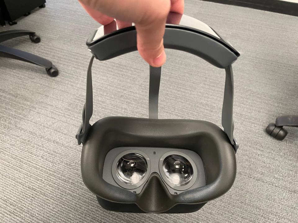 A VR headset hangs by the strap. You can see the inside lenses and face cushion.