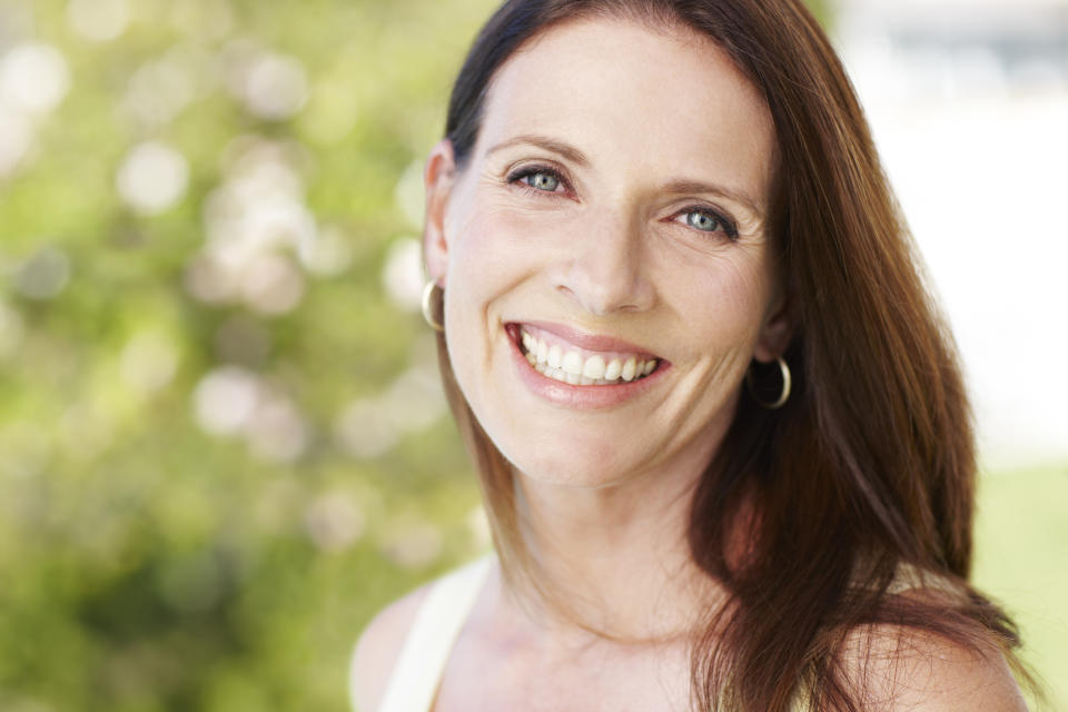 Brunette woman who is outside and is smiling. Her skin looks free of redness after using apple cider vinegar skin care