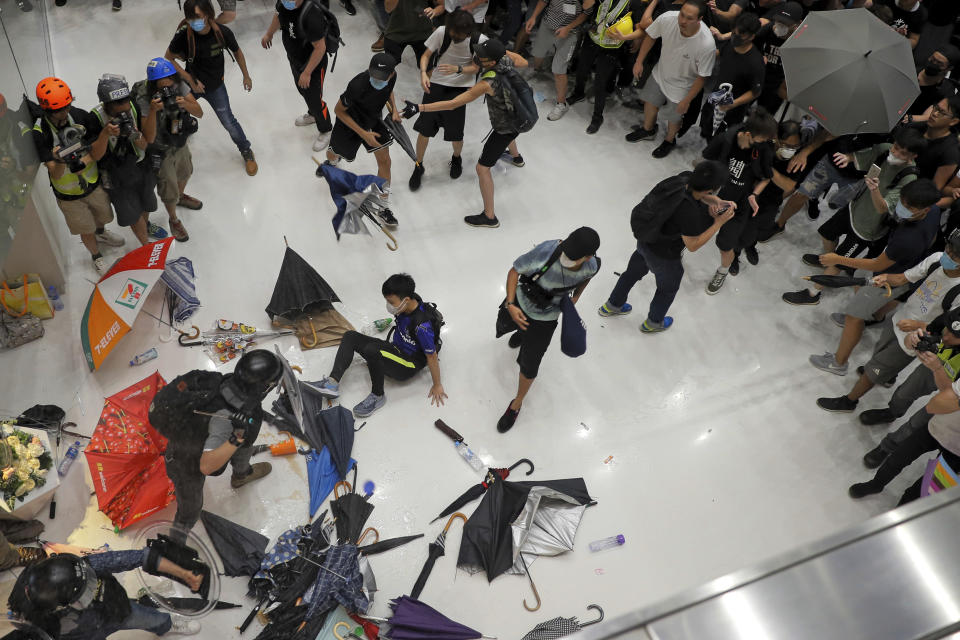 In this Sunday, July 14, 2019, photo, protesters throw umbrellas toward policemen during a crash inside a shopping mall in Sha Tin District in Hong Kong. What began as a protest against an extradition bill has ballooned into a fundamental challenge to the way Hong Kong is governed _ and the role of the Chinese government in the city’s affairs. (AP Photo/Kin Cheung)