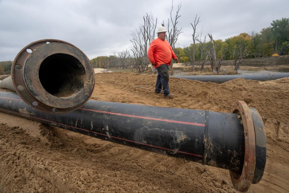 A worker for Newt Marine walks past pipes used to move material that will raise the elevation of an island in the Mississippi River across from Prairie du Chien. The trees in the background were recently killed by flooding, and a U.S. Army Corps of Engineers project will help raise other trees higher above water so they don't meet the same fate.