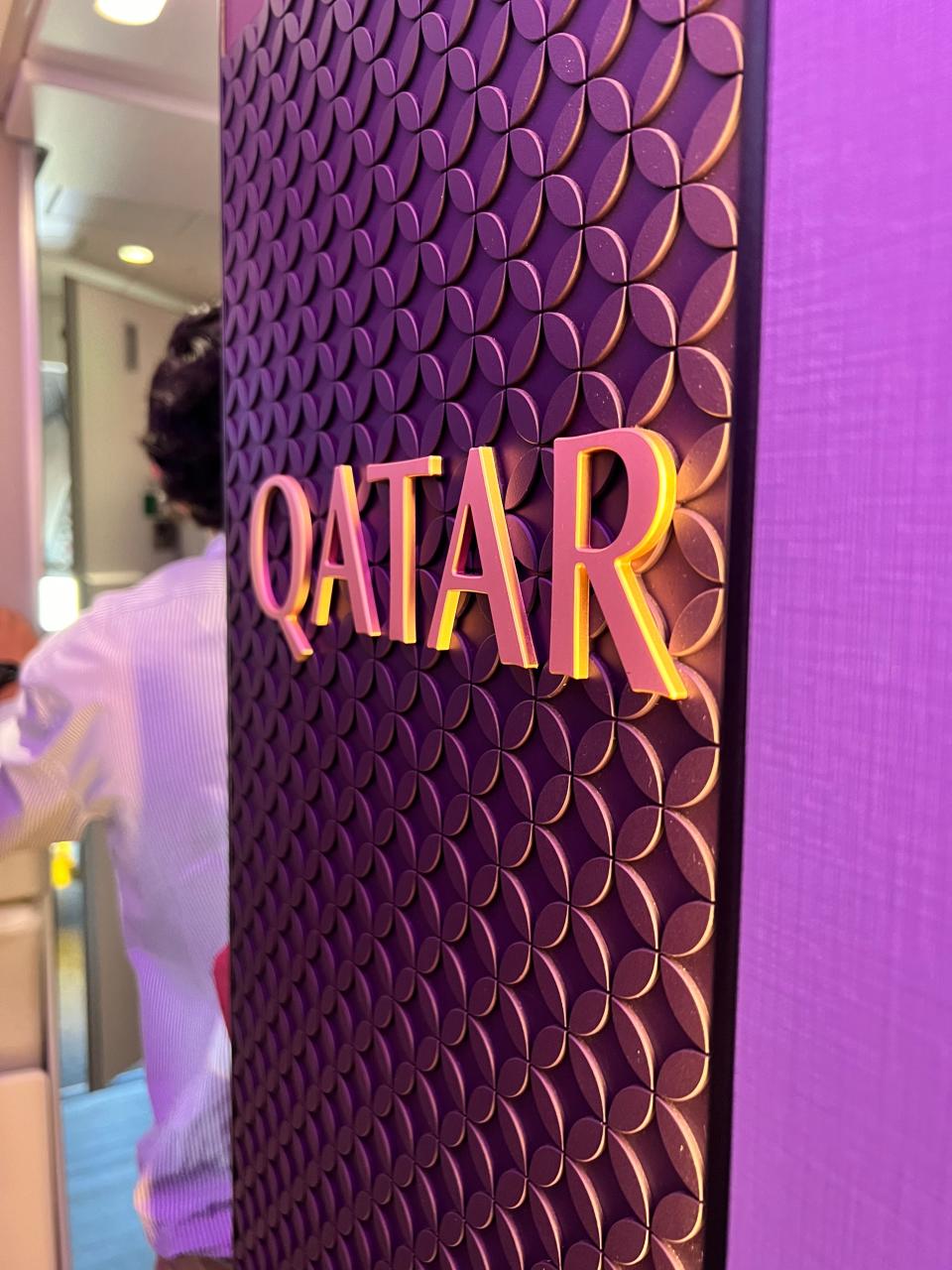 A closeup of the Qatar Airways logo against an ornate brown background.