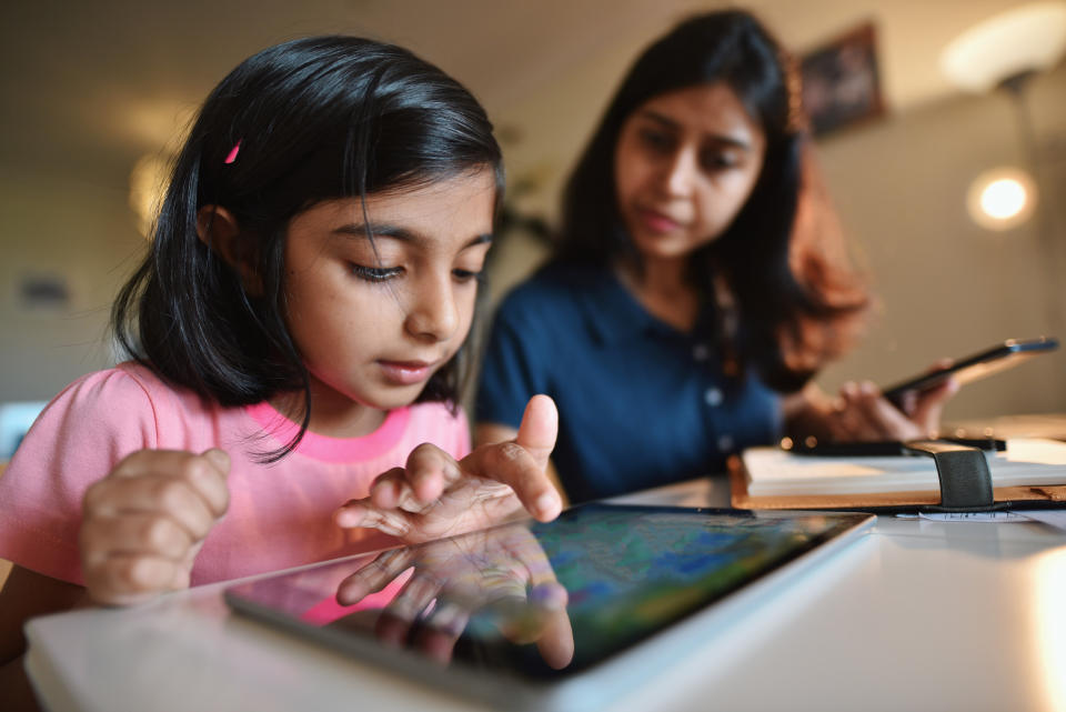 Woman working from home while daughter using digital tablet