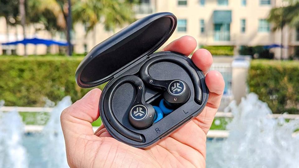 The JLab Epic Air Sport ANC (2nd Gen) wireless earbuds held in hand behind a fountain backdrop