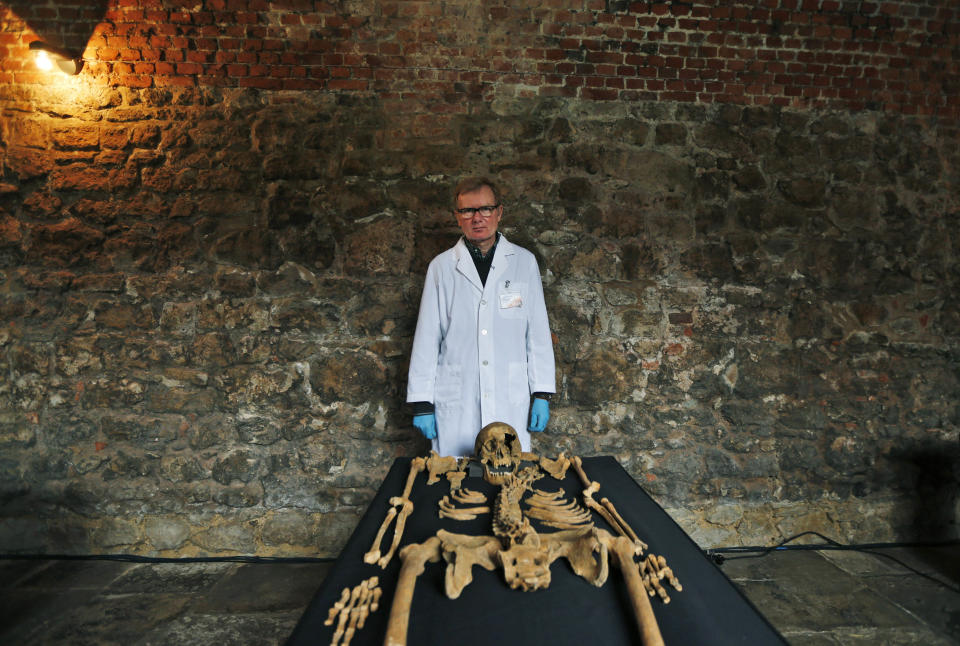 In this Wednesday, March 26, 2014 photo, Don Walker, a human osteologist with the Museum of London, poses for photographers, with one of the skeletons found by construction workers under central London's Charterhouse Square. Twenty-five skeletons were uncovered last year during work on Crossrail, a new rail line that's boring 13 miles (21 kilometers) of tunnels under the heart of the city. Archaeologists immediately suspected the bones came from a cemetery for victims of the bubonic plague that ravaged Europe in the 14th century. The Black Death, as the plague was called, is thought to have killed at least 75 million people, including more than half of Britain's population. (AP Photo/Lefteris Pitarakis)