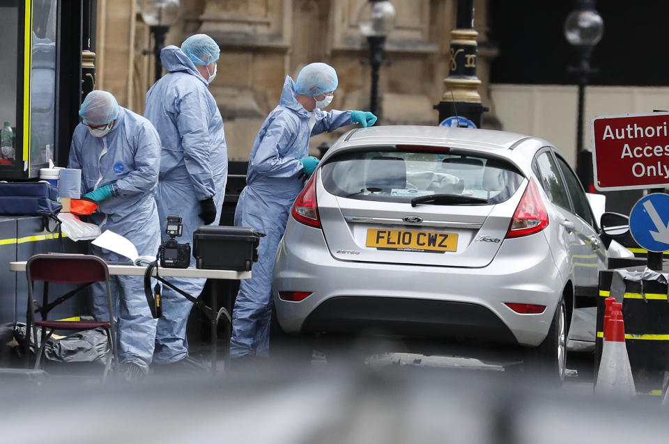 Forensics officers work near the car that crashed into security barriers outside the Houses of Parliament in London, Tuesday, Aug. 14, 2018. Authorities said in a statement Tuesday that a man in his 20s was arrested on suspicion of terrorist offenses after a silver Ford Fiesta collided with a number of cyclists and pedestrians before crashing into the barriers during the morning rush hour. (AP Photo/Frank Augstein)