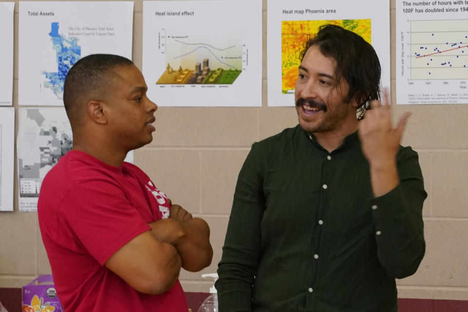 Environmental activist Reggie Carrillo, right, speaks with a community member, Friday, Sept 28, 2022, in Phoenix. Carrillo has benefited from one of several nonprofit initiatives to educate and engage residents about climate fueled heat that disproportionately affects low income neighborhoods of color. (AP Photo/Matt York)