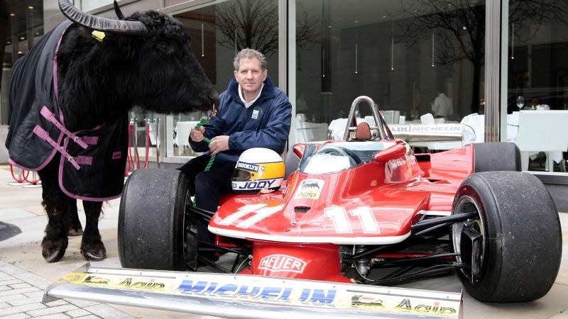 A photo of Jody Scheckter sat on an F1 car holding a cow. 
