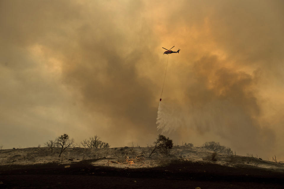 FILE - In this Dec. 9, 2017 file photo, a helicopter drops water while trying to keep a wildfire from jumping Santa Ana Road near Ventura, Calif. An investigation has determined that one of the largest and most destructive fires in California history was sparked by power lines coming into contact during high winds. The Ventura County Fire Department says Wednesday that the contact ignited dry brush on December 4, 2017 and eventually blackened more than 440 square miles (1,139 square kilometers). The Thomas fire destroyed more than a thousand structures in Ventura and Santa Barbara counties and resulted in the deaths of two people. (AP Photo/Noah Berger, File)