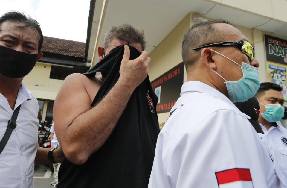 Police officers escort Australian national Aaron Wayne Coyle, center, as he covers his face at the regional police headquarters in Denpasar, Indonesia on Thursday, Sept. 3, 2020. Indonesian police say Coyle and a British national Collum Park have been arrested with methamphetamine and ecstasy pills on the tourist island of Bali. (AP Photo/Firdia Lisnawati)