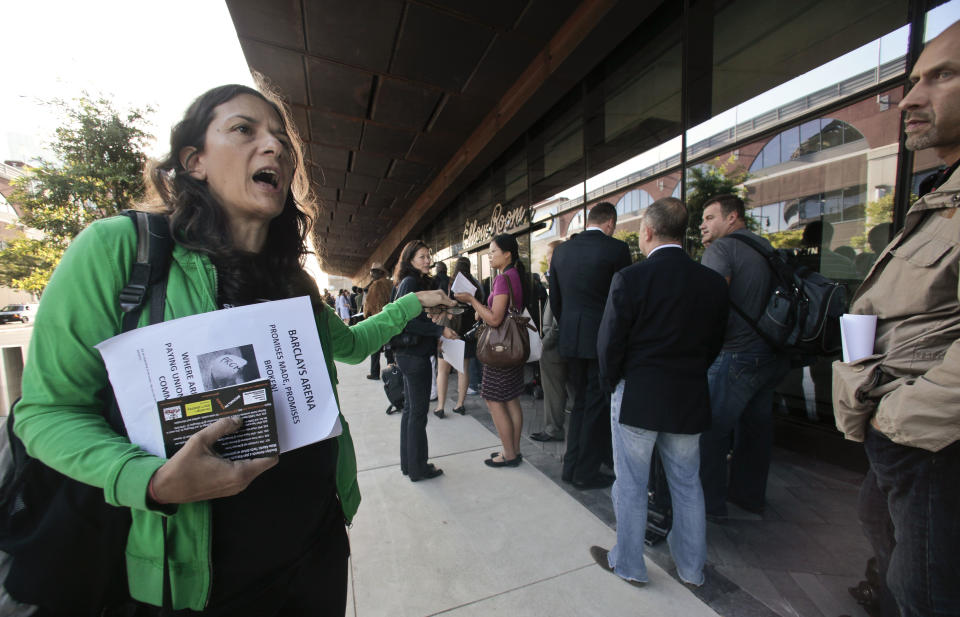 Gloria Mattera announces a press briefing for a coalition of local community groups, as she walks along a line of media entering the Barclays Center, the new arena and home of the Brooklyn Nets NBA basketball team, for a ribbon cutting ceremony on Friday, Sept. 21, 2012 in New York. The coalition says the opening of Barclays Center fulfills the "hoops" part of the Atlantic Yards project, but "mask" the broken promise for jobs and housing used to justify the project. (AP Photo/Bebeto Matthews)