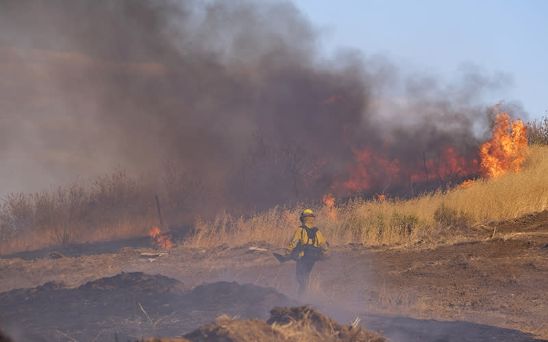 A firefighter walks next to a wildfire burning on a hillside in Castaic, Calif.