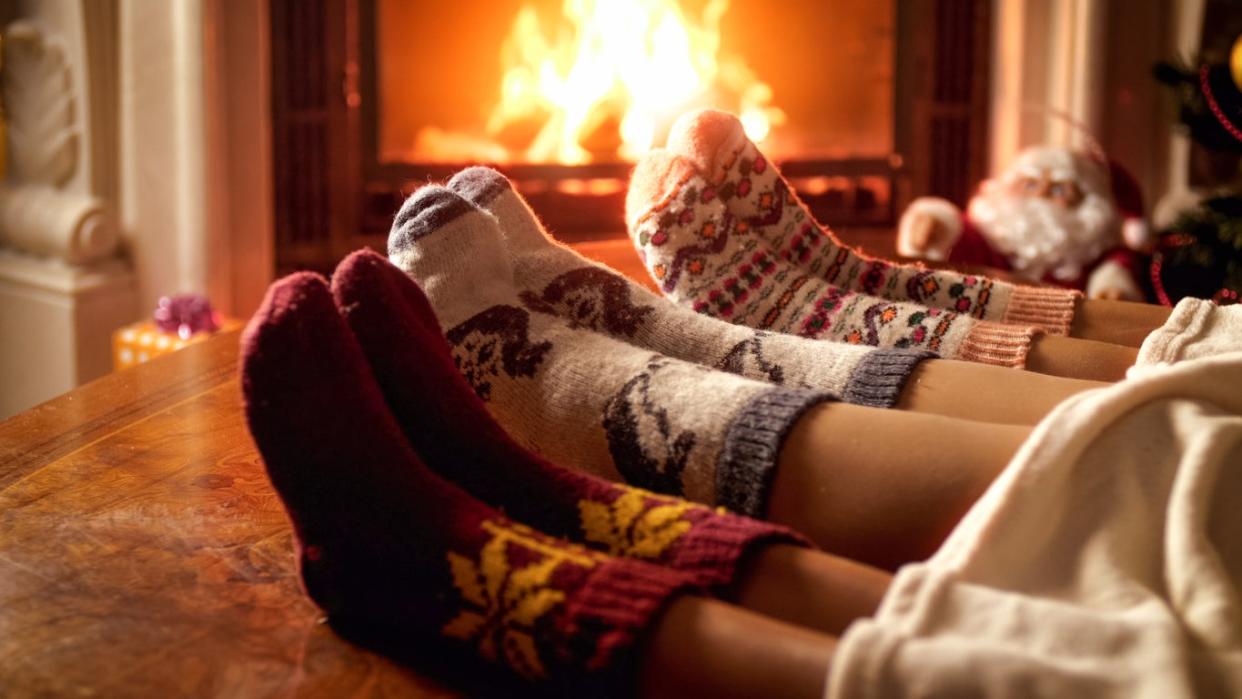 Family in warm knitted socks lying on sofa next to burning fireplace