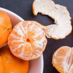 bowl of oranges with one orange partial peeled showing white pith