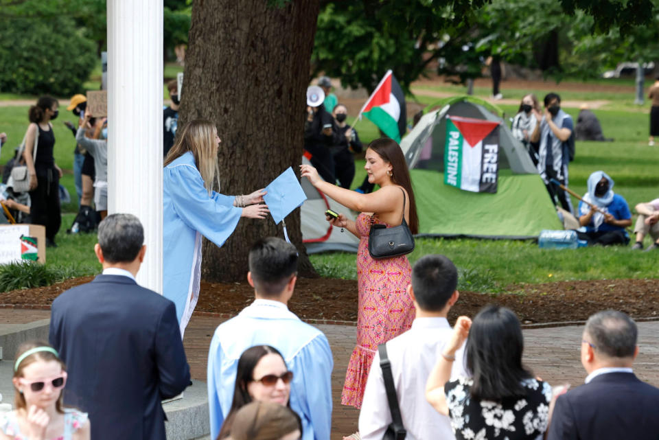 Graduates have their photo taken by the Old Well as pro-Palestinian protesters chant behind them at UNC Chapel Hill on Saturday, May 11, 2024. (Ethan Hyman/The News & Observer via AP)