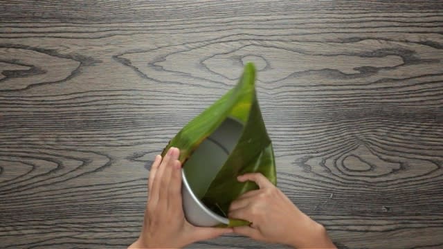 Folding banana leaf down into a round baking tin