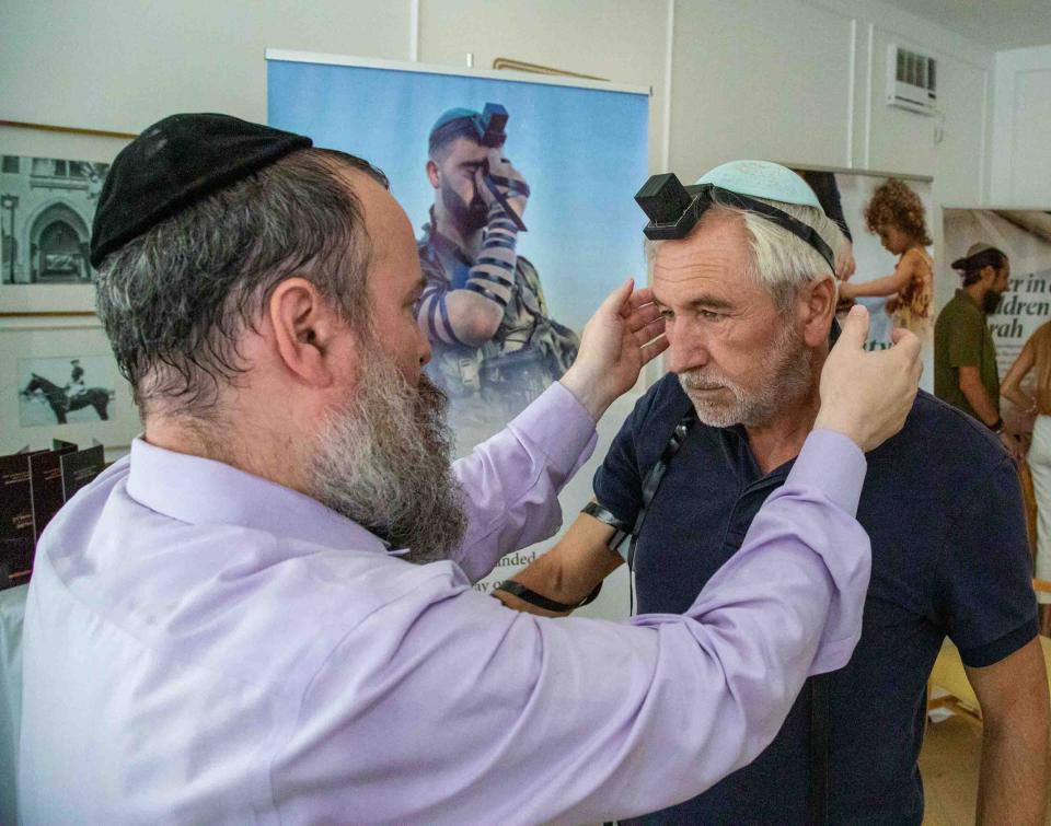 Rabbi Zalman Levitin places a tefillin on the head of Stephan Sportouch at the "A Mitzvah for Israel" pop-up store.