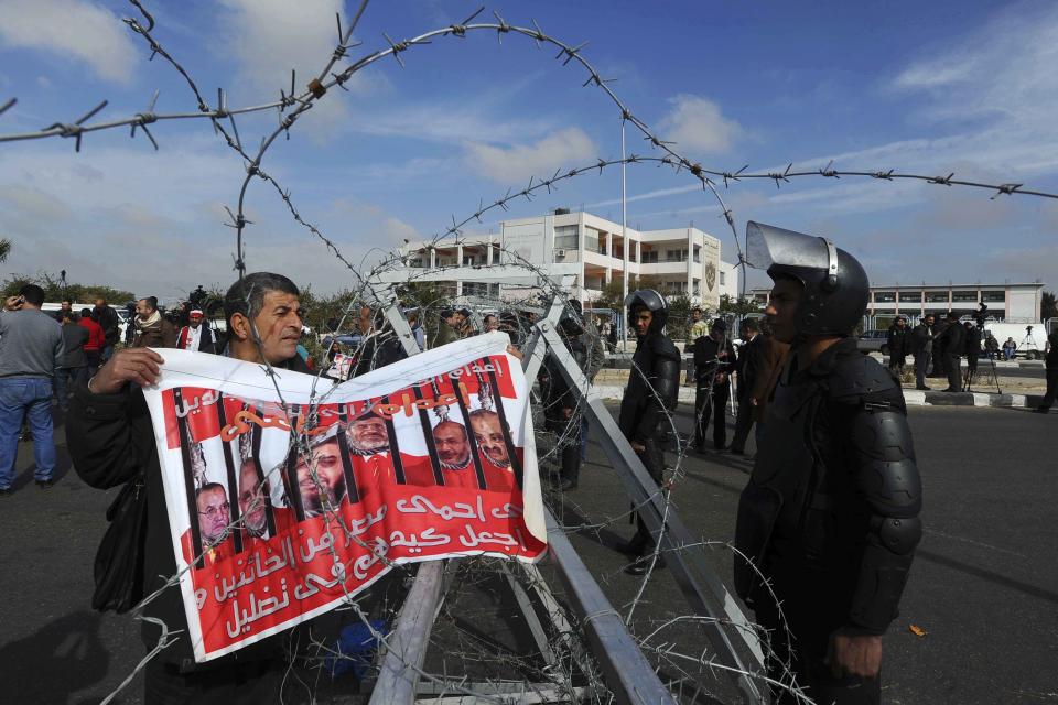 A demonstrator holds an anti-Muslim Brotherhood poster, with ousted Islamist Egyptian President, Mohammed Morsi's photo, center, and other Brotherhood leaders depicted with a noose around their necks, outside a makeshift courtroom at the national police academy, in an eastern suburb of Cairo, Egypt, Saturday, Feb. 1, 2014. The trial of Morsi and 14 others also accused of inciting the killing of protesters resumed on Saturday, Egypt's official news agency reported. The trial is one of four Morsi and top leaders of his Muslim Brotherhood face. The charges levelled against them mostly carry the death penalty. (AP Photo/Ahmed Omar)