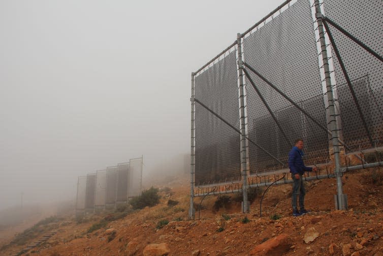 Large nets erected vertically on hillside covered in fog.