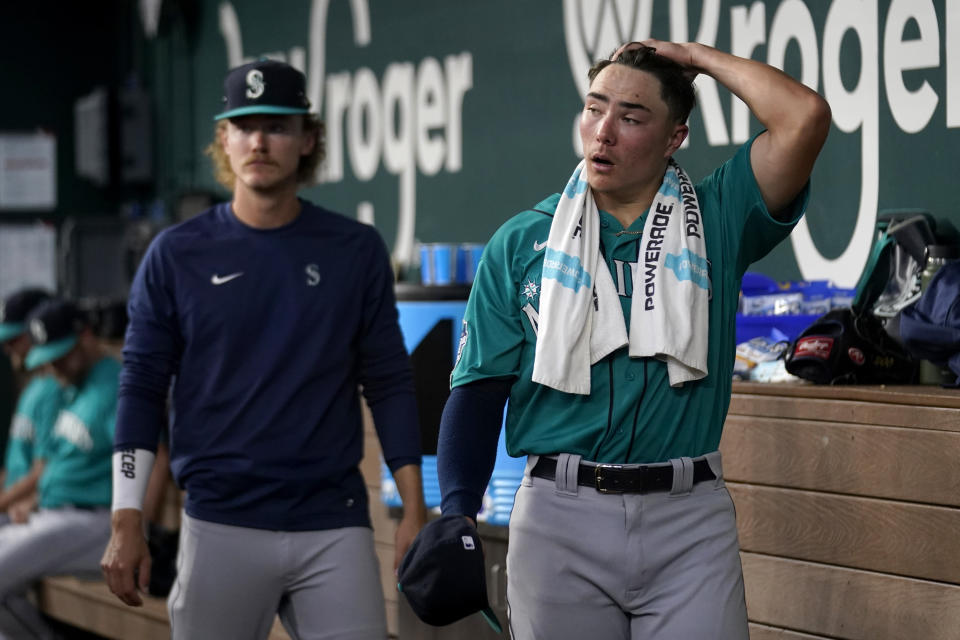 Seattle Mariners starting pitcher Bryan Woo, right, walks through the dugout as he talks with Bryce Miller, left, after working against the Texas Rangers in the second inning of a baseball game, Saturday, June 3, 2023, in Arlington, Texas. Woo threw two innings in his major league debut Saturday. (AP Photo/Tony Gutierrez)