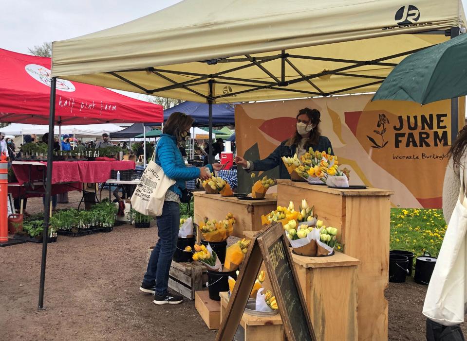 A shopper buys some flowers at the June Farm stall at the Burlington Farmers Market on Pine Street in Burlington on the market's opening day for the year, Saturday, May 8, 2021.