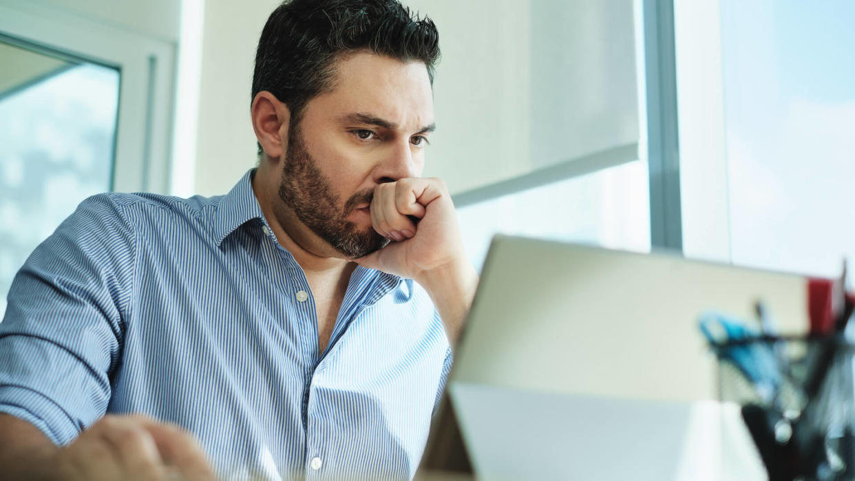 Angry Hispanic businessman working with laptop computer in office, losing patience.