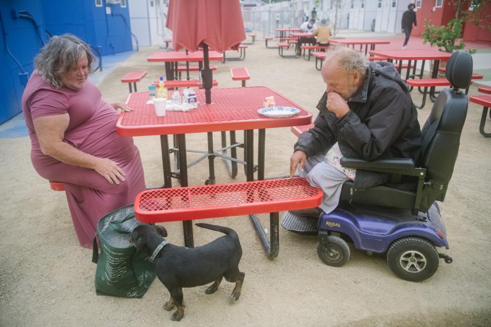Two residents greet a dog while sitting in an area with red tables.