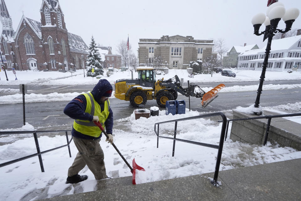 City worker Matt Houle, of Leominster, Mass., left, shovels the steps of Leominster City Hall, Tuesday, March 14, 2023, while a loader, behind, clears the street of snow, in Leominster. The New England states and parts of New York are bracing for a winter storm due to last into Wednesday. (AP Photo/Steven Senne)