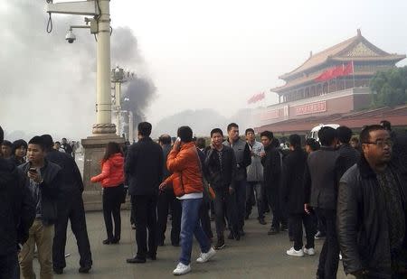 People walk along the sidewalk of Chang'an Avenue as smoke rises in front of the main entrance of the Forbidden City at Tiananmen Square in Beijing in this October 28, 2013 file photo. REUTERS/Stringer/Files