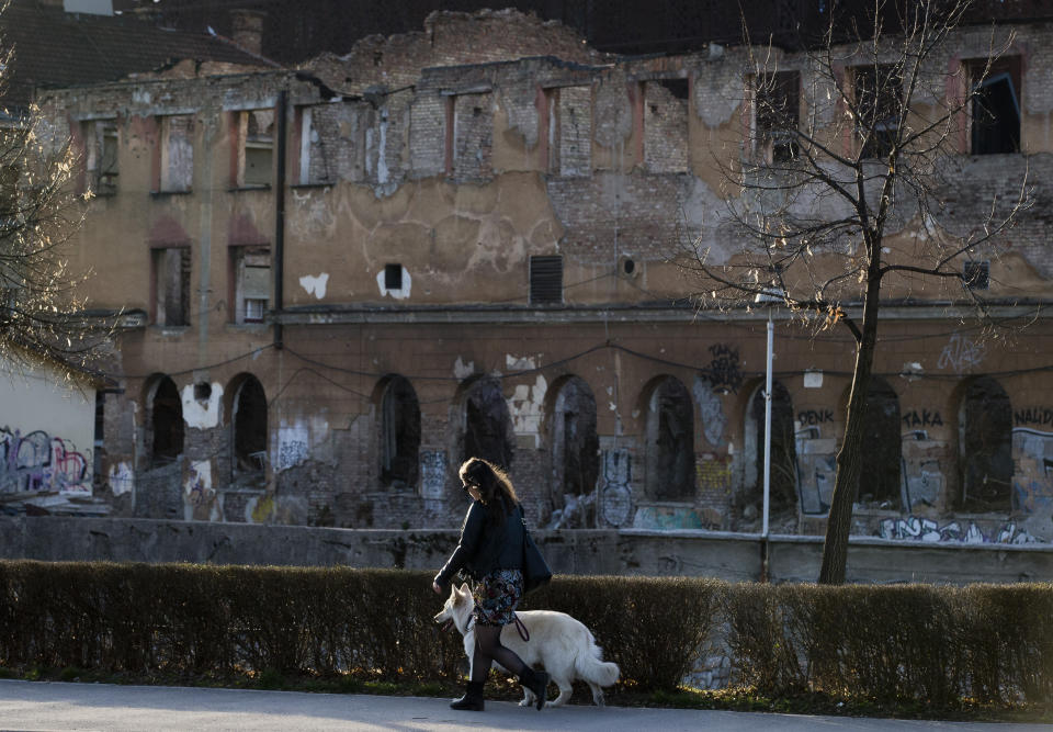 In this Sunday, March 17, 2019 photo, a woman walks a dog past a war damaged building in Sarajevo, Bosnia-Herzegovina. Nearly a quarter of a century since Bosnia's devastating war ended, former Bosnian Serb leader Radovan Karadzic is set to hear the final judgment on whether he can be held criminally responsible for unleashing a wave of murder and mistreatment by his administration's forces. United Nations appeals judges on Wednesday March 20, 2019 will decide whether to uphold or overturn Karadzic's 2016 convictions for genocide, crimes against humanity and war crimes and his 40-year sentence. (AP Photo/Darko Bandic)