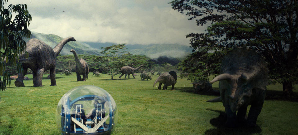 A gyrosphere rolling across a green space with dinosaurs