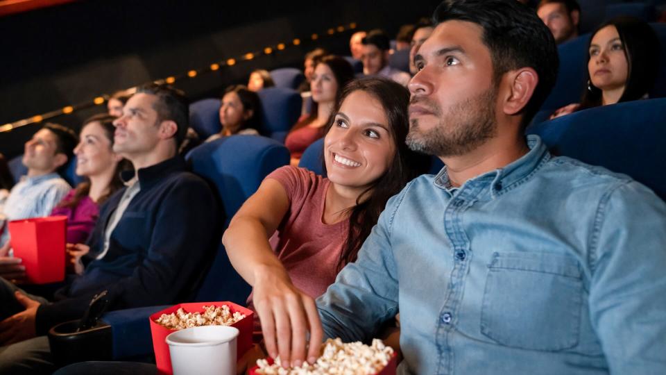 Portrait of a happy couple at the movies and woman stealing popcorn from her boyfriend - entertainment concepts.