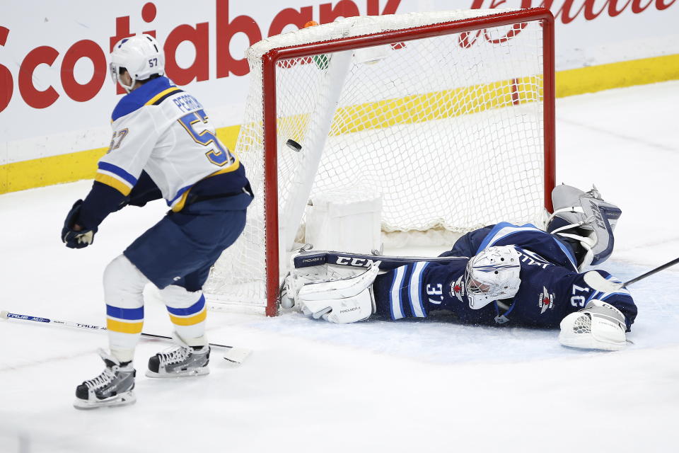 St. Louis Blues' David Perron (57) scores the winning goal in overtime against Winnipeg Jets goaltender Connor Hellebuyck (37) in NH hockey game action in Winnipeg, Manitoba, Friday, Dec. 27, 2019. (John Woods/The Canadian Press via AP)