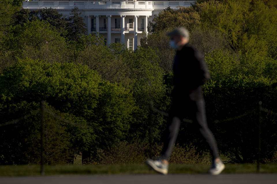 The White House is visible as a man wearing a mask makes his way across the National Mall, Wednesday, April 22, 2020, in Washington. Amid pockets of attention-grabbing protests, a new survey finds Americans remain overwhelming in favor of stay-at-home orders and other efforts to slow the spread of coronavirus. (AP Photo/Andrew Harnik)