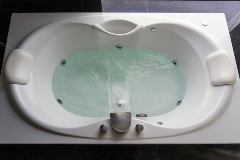 empty white massaging jetted bathtub with turquoise water on black polished stone floor