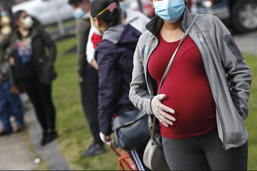 FILE - In this May 7, 2020 file photo, a pregnant woman wearing a face mask and gloves holds her belly as she waits in line for groceries at St. Mary's Church in Waltham, Mass. The Centers for Disease Control and Prevention urged all pregnant women Wednesday, Aug. 11, 2021 to get the COVID-19 vaccine as hospitals in hot spots around the U.S. see disturbingly high numbers of unvaccinated mothers-to-be seriously ill with the virus. (AP Photo/Charles Krupa, file)