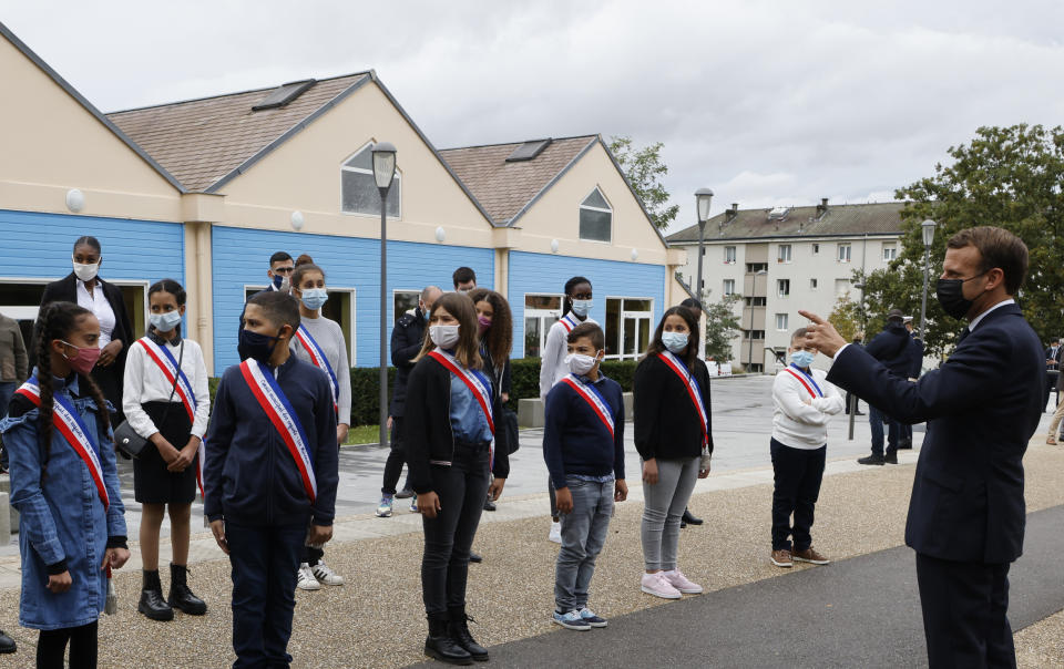 French President Emmanuel Macron, right, wearing a protective face mask speaks to youngsters standing in line outside the 'la Maison des habitants' (MDH) in Les Mureaux, northwest of Paris, Friday, Oct. 2, 2020. President Emmanuel Macron, trying to rid France of what authorities say is a "parallel society" of radical Muslims thriving outside the values of the nation, is laying the groundwork Friday for a proposed law aimed at helping remedy the phenomenon. (Ludovic Marin / Pool via AP)