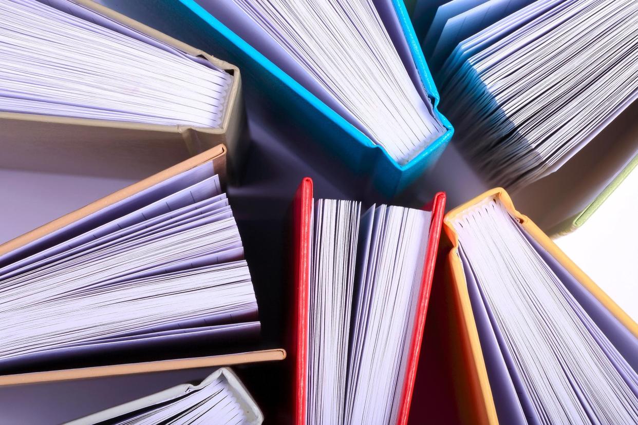 Top view of seven books scattered, pages looking like fans, against a white background