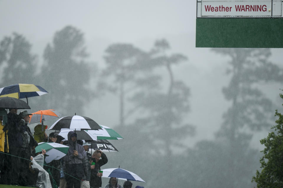 Patrons line the fairway in the rain on the 18th hole during the weather delayed second round of the Masters golf tournament at Augusta National Golf Club on Saturday, April 8, 2023, in Augusta, Ga. (AP Photo/Charlie Riedel)