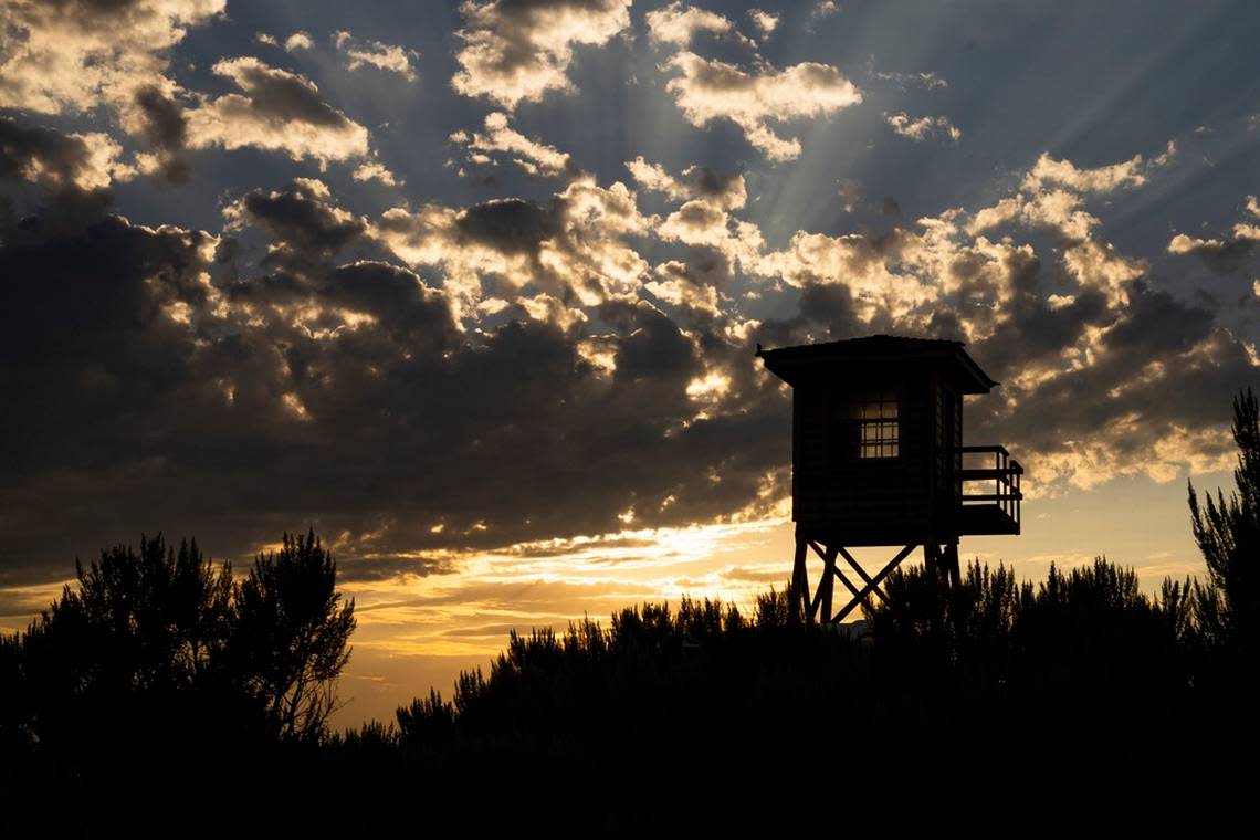 A reconstructed entry guard tower is silhouetted by the sunset. The original tower was one of eight such structures manned by United States military on the site surrounded by miles of barbed wire.