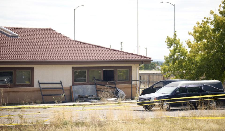 Two cars sit behind crime scene tape in front of a single story building with a tile roof