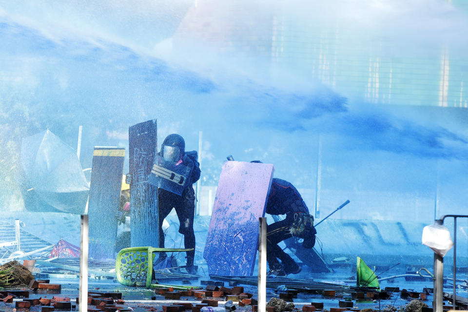 Protestors duck behind shields as a blue-dyed liquid is sprayed from an armored police vehicle at the Hong Kong Polytechnic University in Hong Kong, Sunday, Nov. 17, 2019. (AP Photo/Achmad Ibrahim)