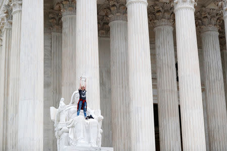 A protester stands on the lap of "Lady Justice" on the steps of the U.S. Supreme Court building holding up a "Believe Survivors" sign as demonstrators storm the steps and doors of the Supreme Court while Judge Brett Kavanaugh is being sworn in as an Associate Justice of the court inside on Capitol Hill in Washington, U.S., October 6, 2018. REUTERS/Carlos Barria