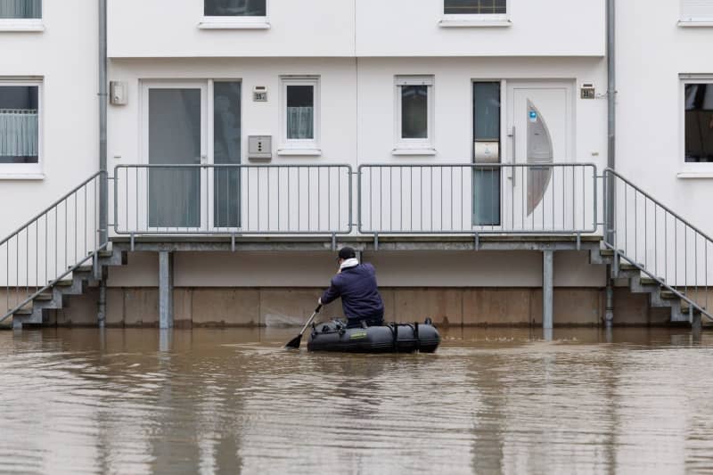 A man sits in a rubber dinghy and paddles to a house that is standing in the water. The water level of the Weser has risen significantly over the past few days. Friso Gentsch/dpa