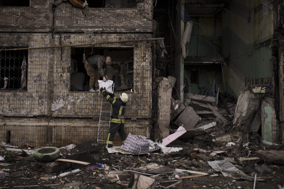 A Ukrainian firefighter helps a man remove belongings from a destroyed building after it was hit by artillery shelling in Kyiv, Ukraine, Monday, March 14, 2022. (AP Photo/Felipe Dana)