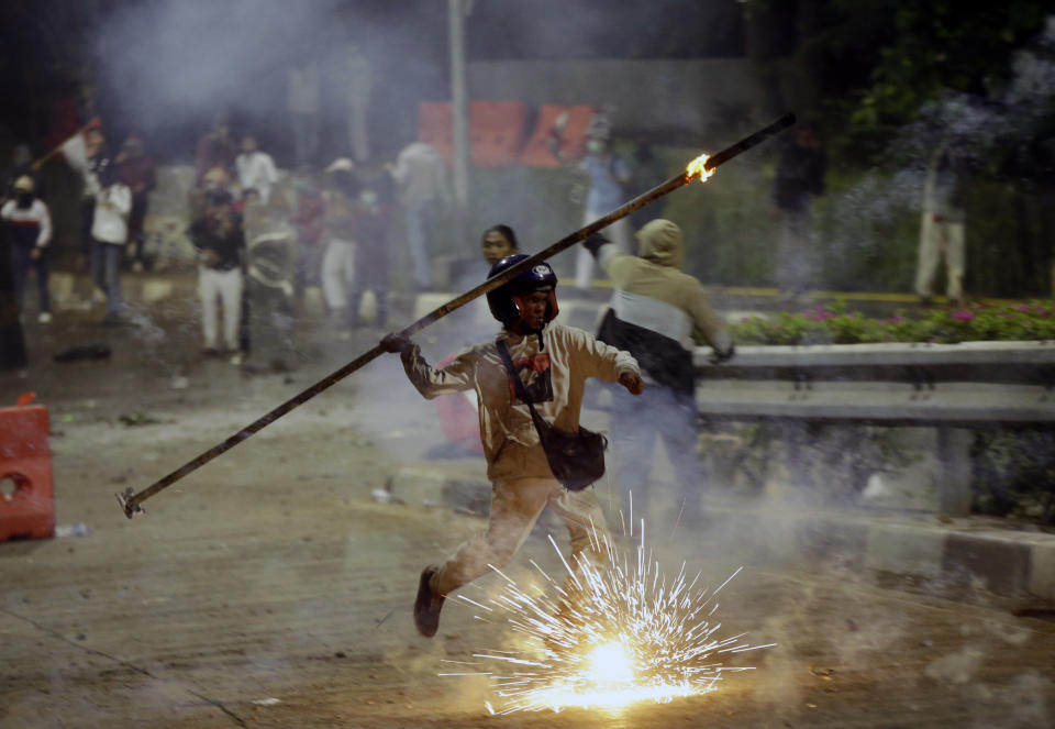 A student protester throws a burning stick at riot police officers during a clash in Jakarta, Indonesia, Monday, Sept. 30, 2019. Thousands of Indonesian students resumed protests on Monday against a new law they say has crippled the country's anti-corruption agency, with some clashing with police.(AP Photo/Achmad Ibrahim)